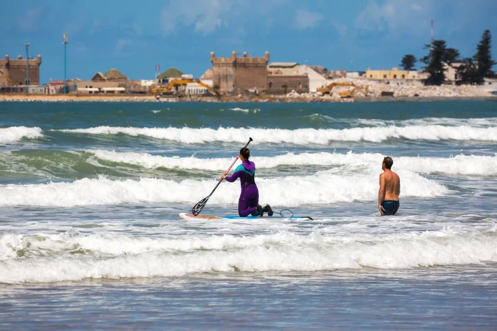Woman practicing stand-up paddle near the shore in Essaouira, Morocco with historic fortress in the background