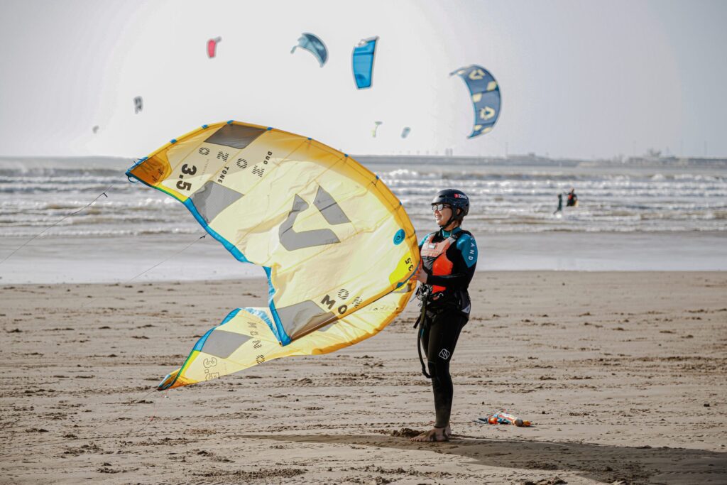 Kitesurf student handling a yellow kite on the beach in Essaouira with multiple kites flying in the background