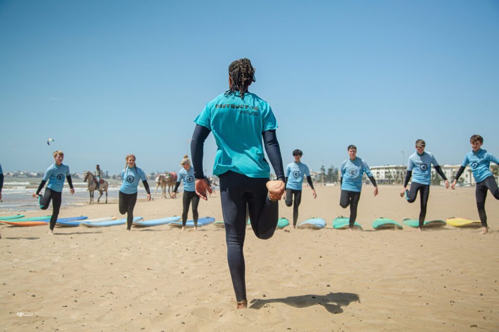 Surf instructor leading a warm-up session with students on the beach of Essaouira before their lesson