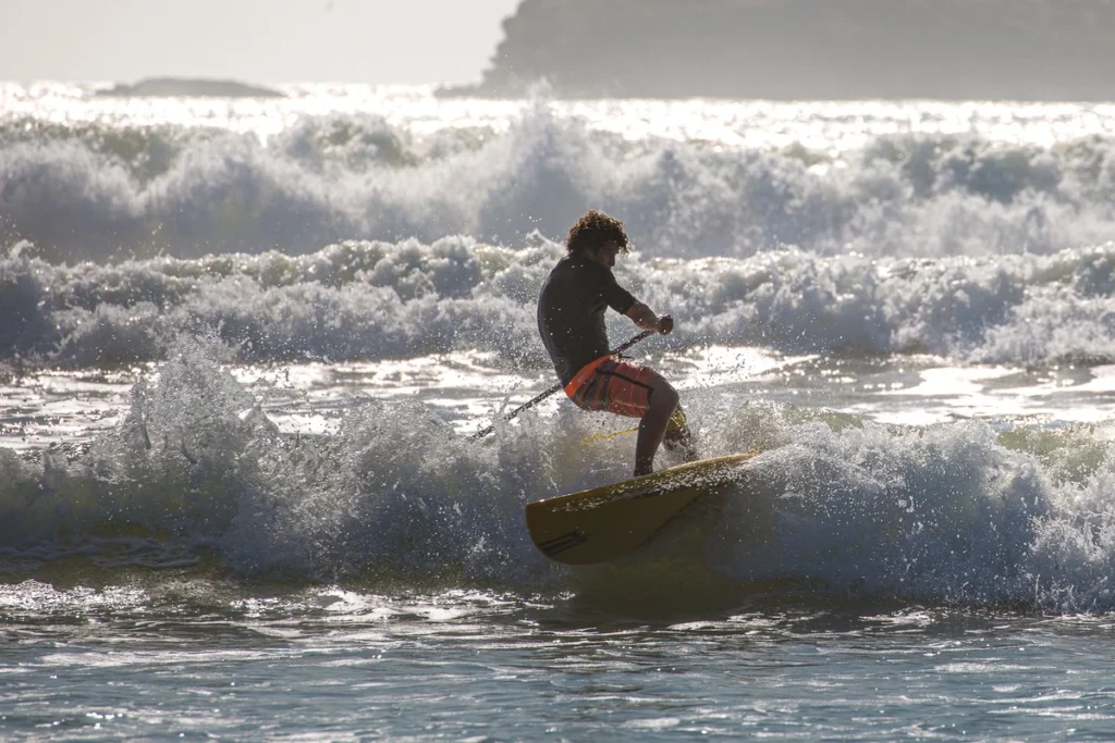 Stand-up paddle surfer riding a wave in Essaouira, Morocco during sunset light